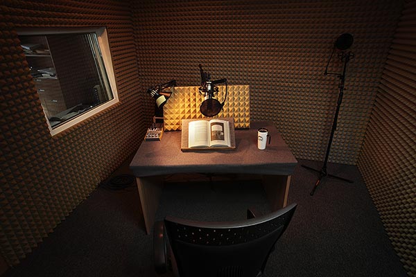 Zdjęcie przedstawia pomieszczenie studia nagrań z biurkiem, i dobrze oświetloną książką.
