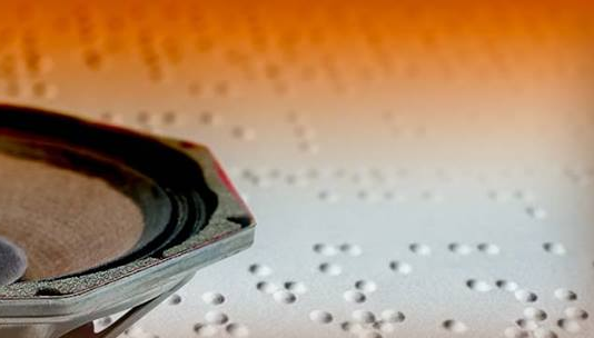 Zdjęcie przedstawiające głośnik na białej karcie zapisanej pismem Braille'a